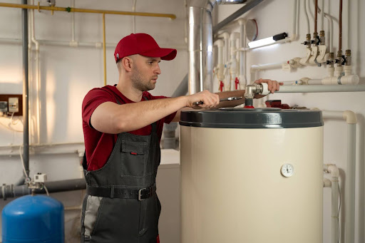 A man performing a service on a traditional tank water heater.