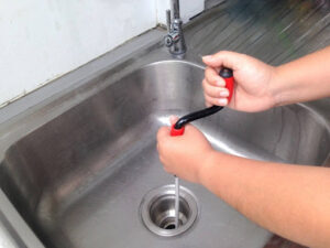 Hand cranking drain snake in kitchen sink drain.