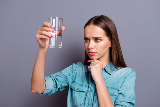 Woman looking at water glass questioningly.